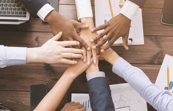 Diverse employees all places their hands on top of one another