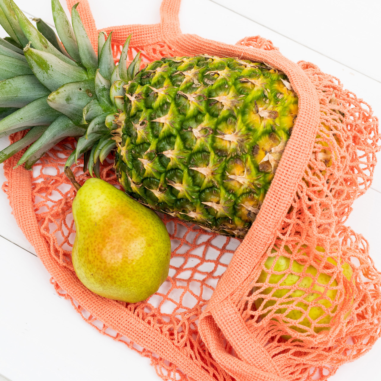 A pineapple and pears in a pink reusable grocery bag